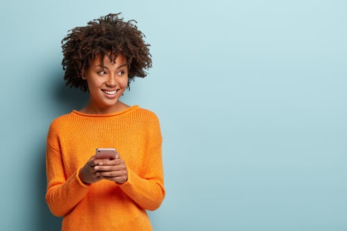 A smiling woman in an orange sweater holding an iPhone