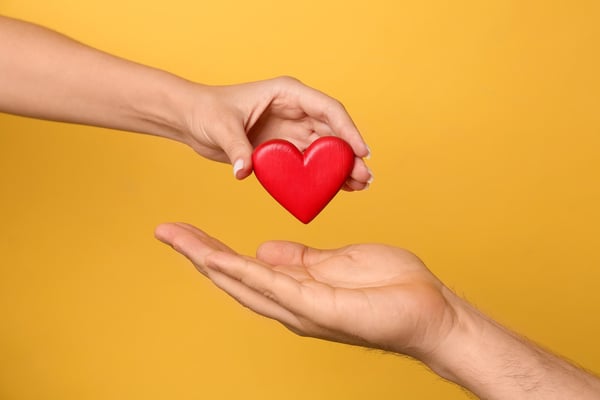 Woman giving red heart to man on yellow background