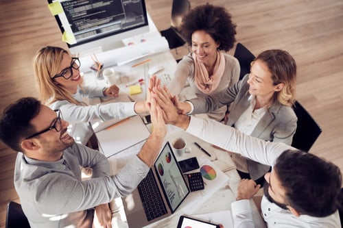group of people giving high fives to each other around a table