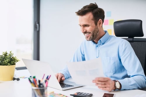 Businessman in his office and smiling while looking at his laptop