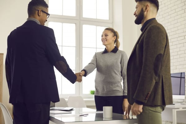 volunteer management: Smiling woman shaking hands with a man while her colleague stands beside her