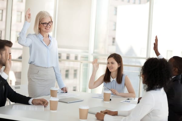 volunteer management: Four people raising their hands during a team meeting